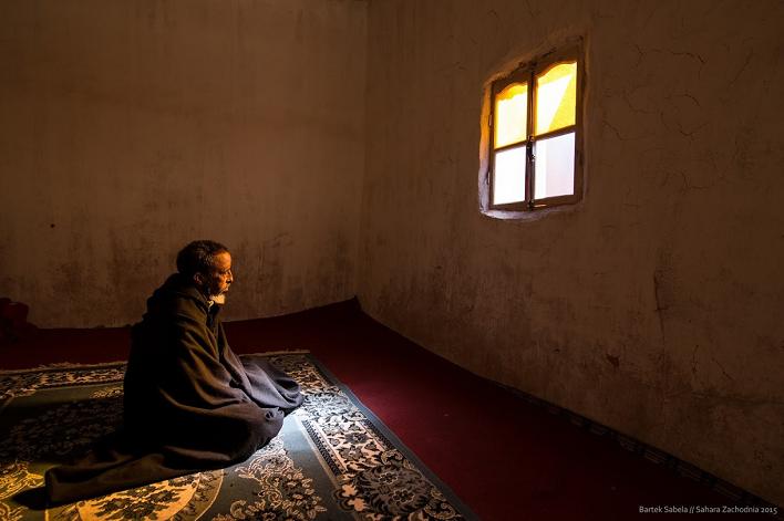 Zdjęcie osoby siedzącej na dywanie w pustym pokoju przed oknem, z którego idzie silne światło słoneczne