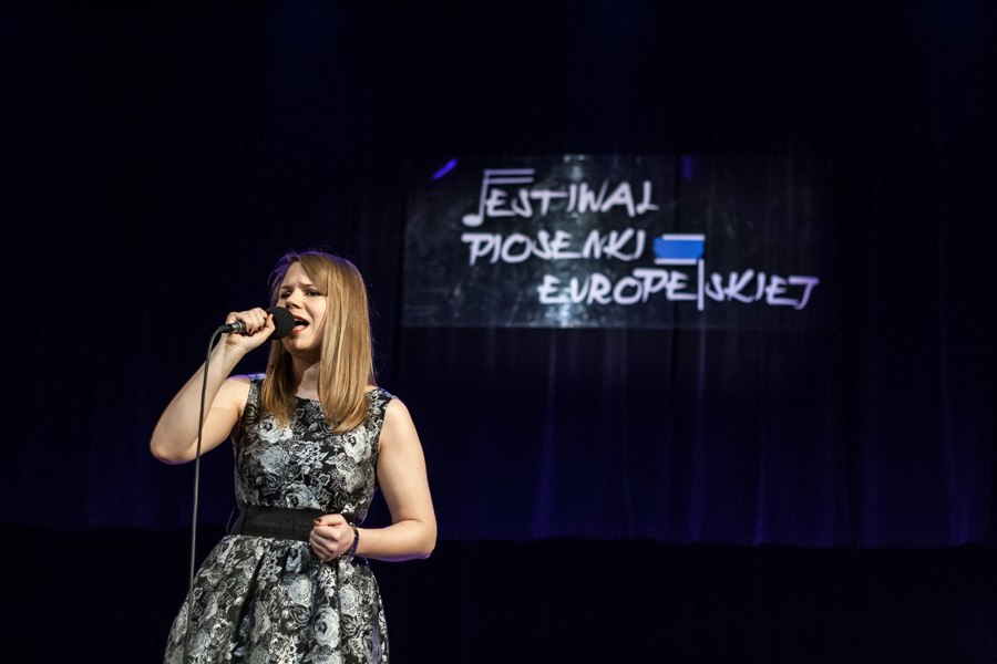 Kobieta w szarej sukience śpiewająca do mikrofonu
