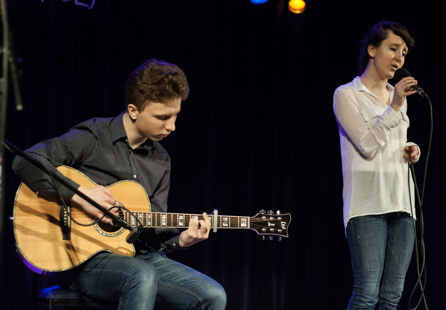 Mężczyzna grający na gitarze, obok niego kobieta śpiewająca do mikrofonu