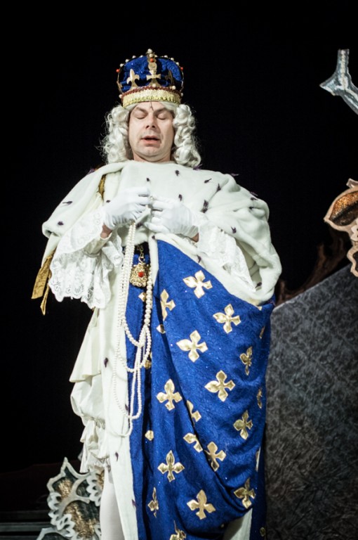 Mężczyzna przebrany za króla w niebiesko-złotych szatach przemawia na scenie