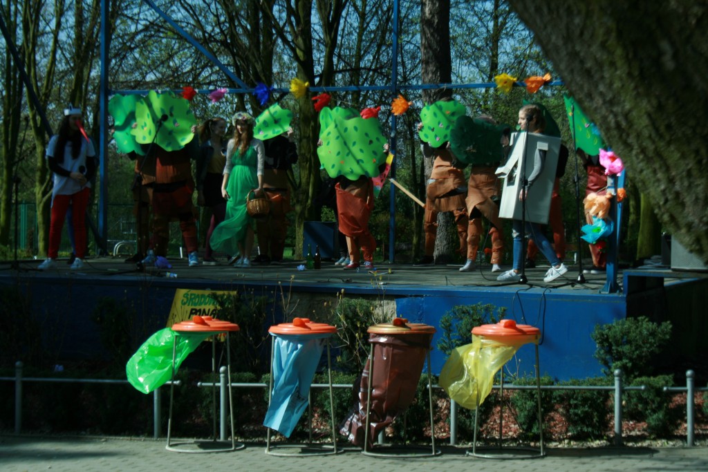 Występujący na scenie w parku trzymający duże sztuczne liście