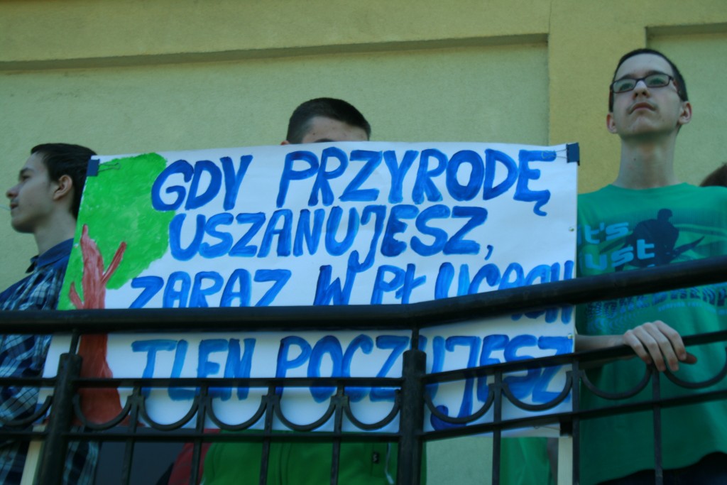 Dzieci przed domem kultury trzymające baner z napisem 'Gdy Przyrodę Uszanujesz Zaraz W Płucach Tlen Poczujesz'