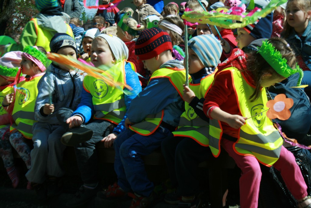 Zbliżenie na widownie dzieci, prawie wszystkie mają ubrane kamizelki odblaskowe, trzymają patyki z owinięta na nich kolorową bibułą