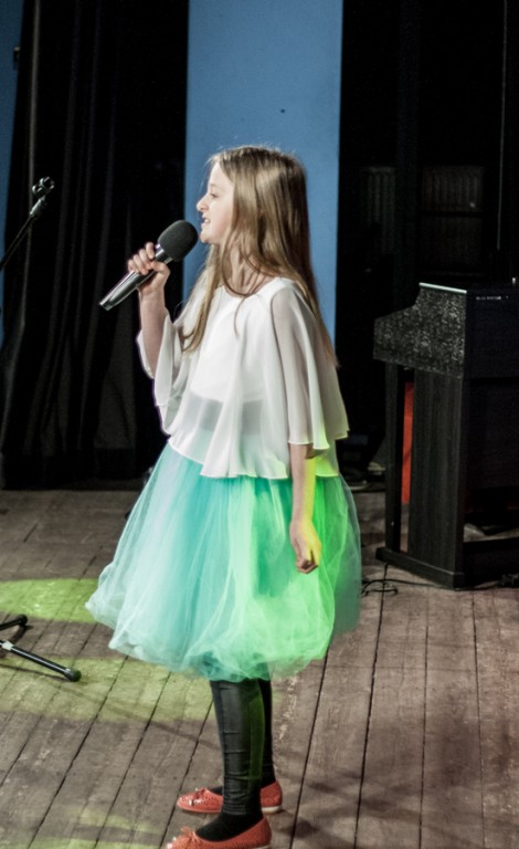 Dziewczynka w zielonej spódnicy śpiewa do mikrofonu