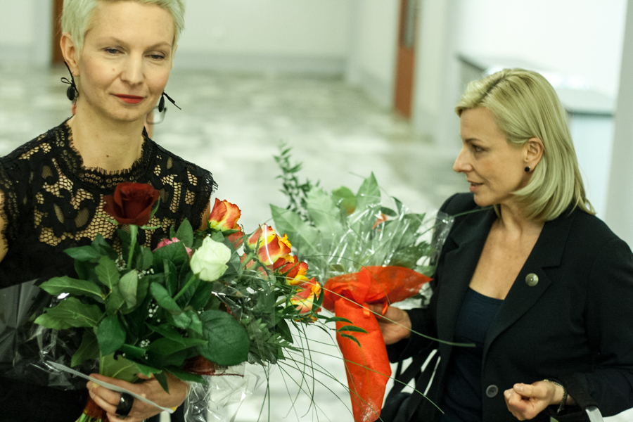 Dwie kobiety w białej sali trzymające bukiety kwiatów