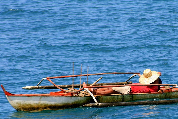 Człowiek z twarzą zakrytą kapeluszem leżący na łodzi dryfującej po błękitnej wodzie