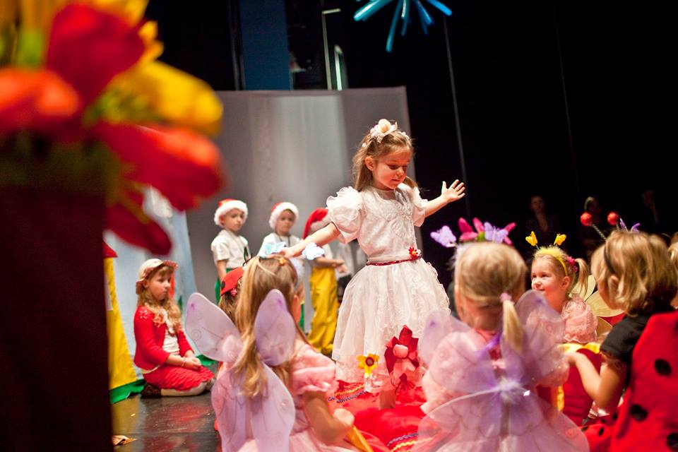 Dzieci poprzebierane za owady stoją wokół dziewczynki w białej sukience na scenie