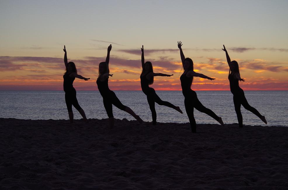 Sylwetki tańczących kobiet na piasku przy morzu podczas zachodu słońca