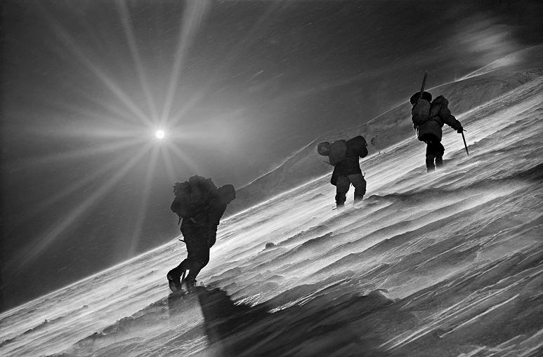 Czarno-białe zdjęcie trzech osób idących pod górę po śnieżnym terenie