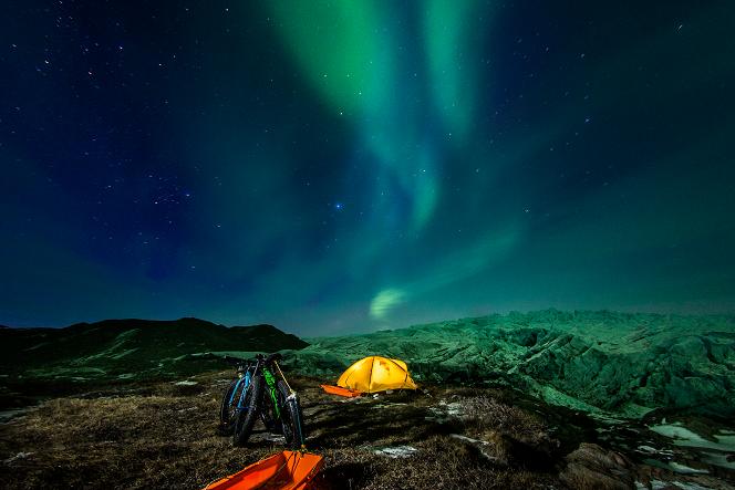 Namioty na górzystym terenie w nocy, na niebie zorza polarna