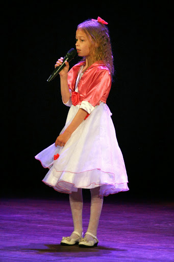 Dziewczynka w różowej kokardzie śpiewa na scenie