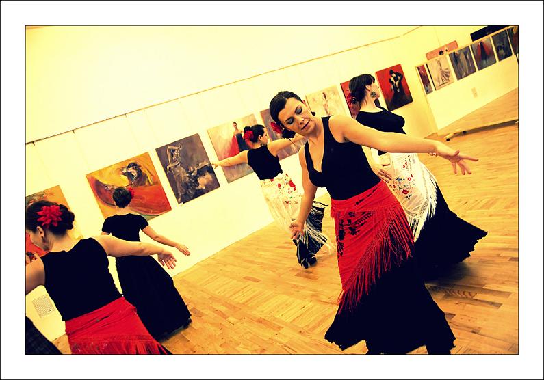 Tańczące kobiety w hiszpańskich strojach, za nimi galeria obrazów na ścianach