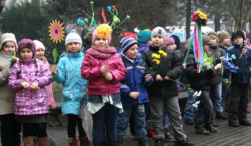 Dzieci w kurtkach stoją na dworze i trzymają różne kwiaty i dekoracje
