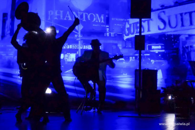 Czarne sylwetki zespołu muzycznego grającego na scenie oświetlonej na niebiesko