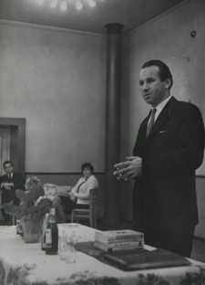 mężczyzna w garniturze przemawiający przed stołem