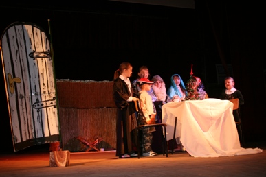 Dzieci na scenie stoją przy stole pokrytym białym obrusem