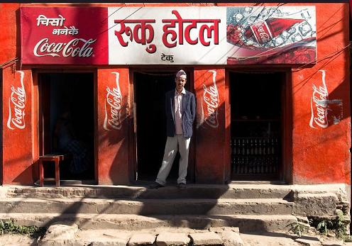 Mężczyzna stoi przed wejściem do budynku oklejonego logiem Coca-Coli
