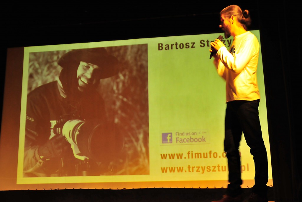 Osoba przemawiająca do mikrofonu, za nią na prezentacji zdjęcie mężczyzny podpisane 'Bartosz'