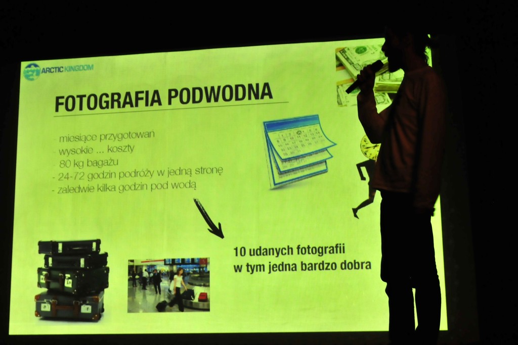 Osoba mówiąca do mikrofonu, za nią prezentacja o fotografii podwodnej