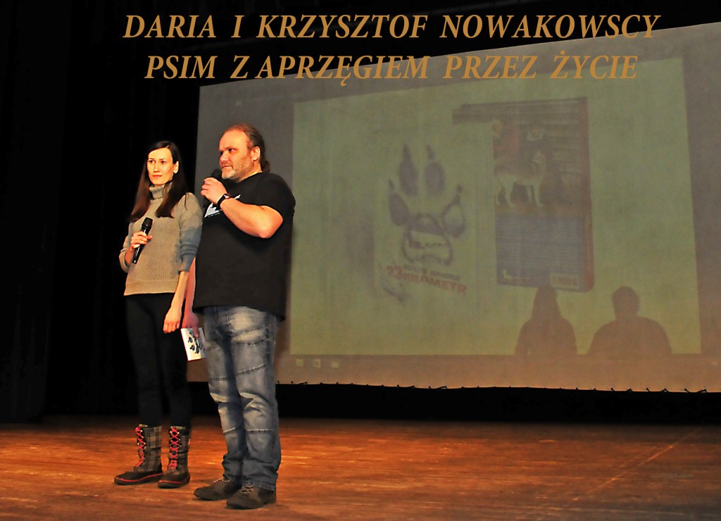 Para osób na scenie, przy nich napis 'Daria i Krzysztof Nowakowscy psim zaprzęgiem przez życie'