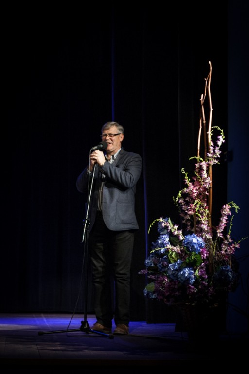 Mężczyzna mówiący do mikrofonu, przy nim kwiaty