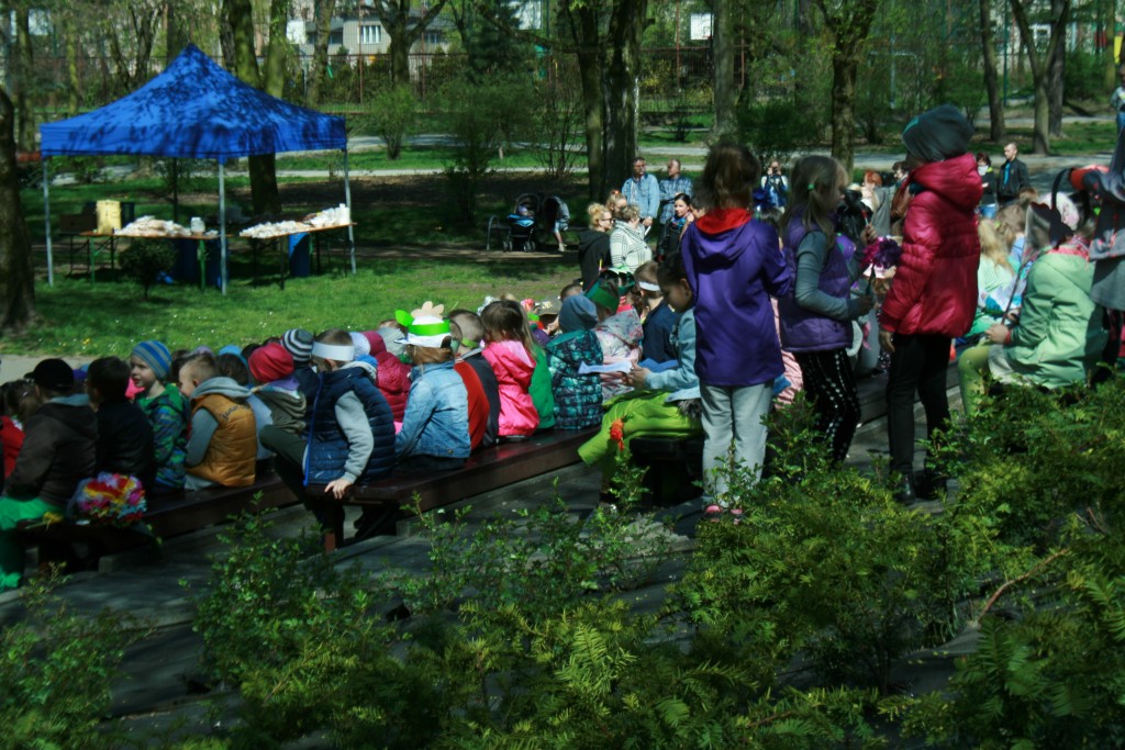 Widownia dzieci w parku, niedaleko oddalone od nich jest niebieskie stoisko