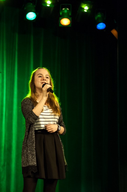 Dziewczyna śpiewająca do mikrofonu, za nią zielona kurtyna