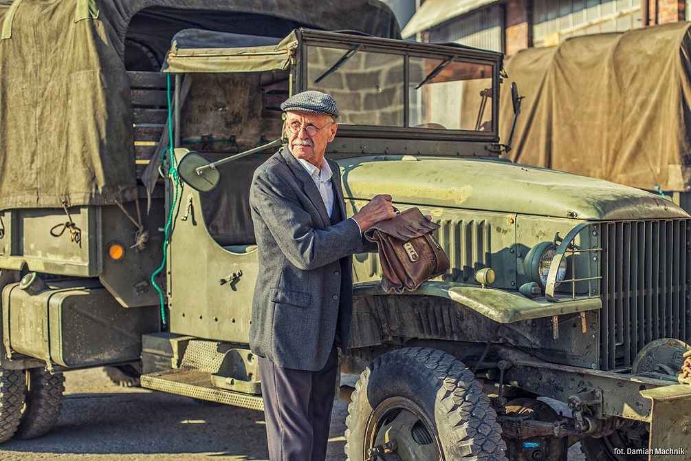 Starszy mężczyzna elegancko ubrany na tle starej ciężarówki