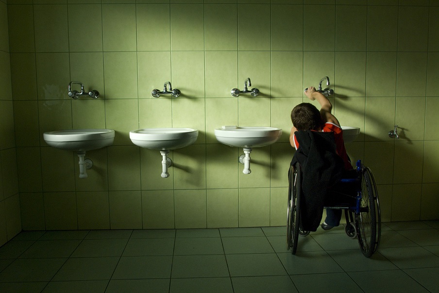 Osoba na wózku odkręcająca kran w publicznej toalecie