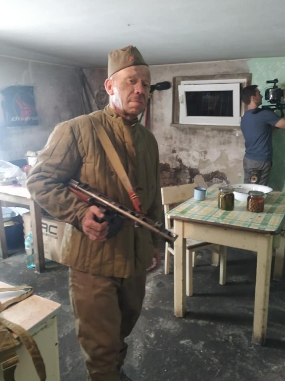Żołnierz z bronią w starej kuchni i mężczyzna ustawiający kamerę