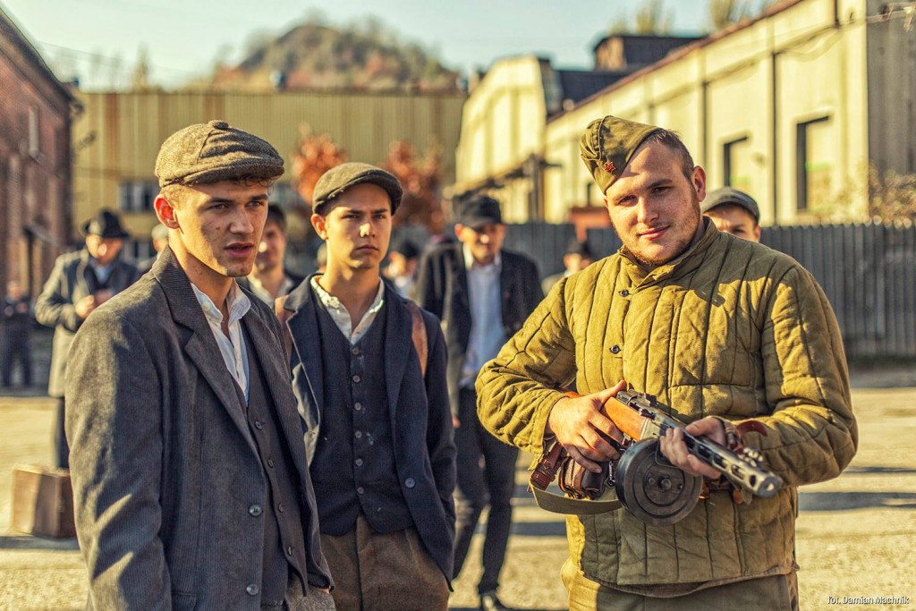Mężczyzna z radziecką czapką i bronią, obok mężczyźni z kaszkietami