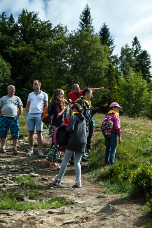 Dzieci z rodzicami na dróżce przed lasem, przewodnik wskazuje palcem w oddal