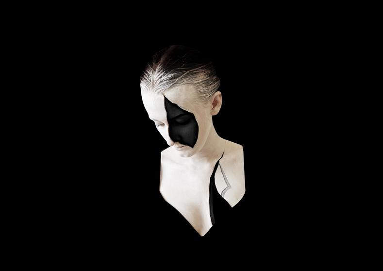 Osoba z pomalowanym na twarzy czarnym akcentem, zakryta od piersi i barku czarnym materiałem wtapiającym się w czarne tło