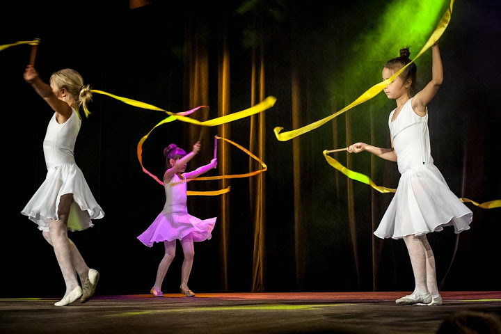 Dziewczynki ubrane w sukienki tańczące z żółtymi wstęgami na scenie