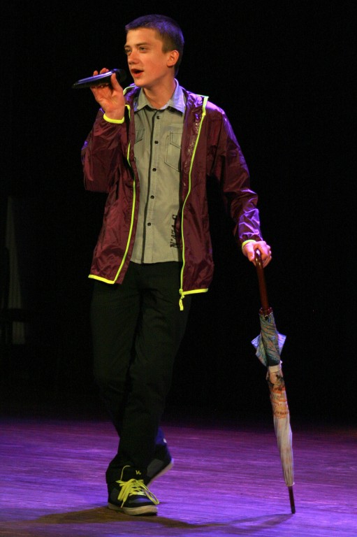 Mężczyzna na scenie opierając się o parasol rozmawia do mikrofonu