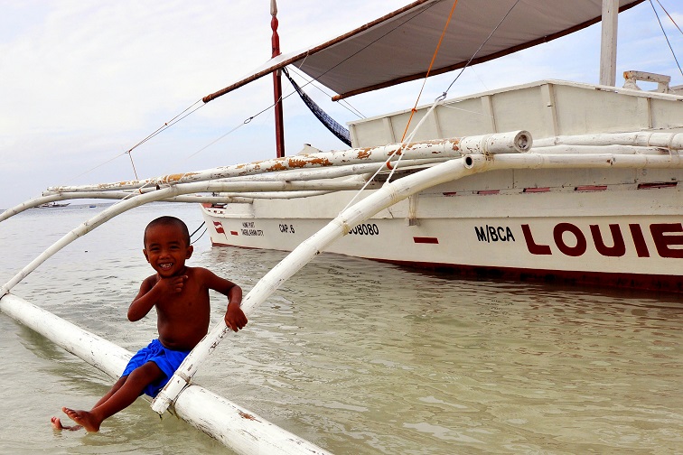 Ciemnoskóre dziecko siedzące na belce wystającej z łodzi nad wodą