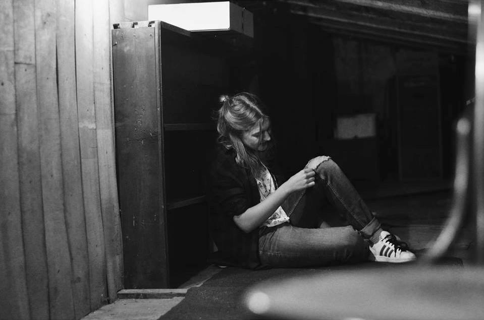 Czarno-białe zdjęcie dziewczyny siedzącej na ziemi przed pustą komodą