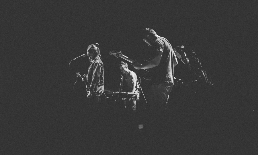 Czarno-białe zdjęcie występującego zespołu muzycznego, który zlewa się z ciemnym tłem