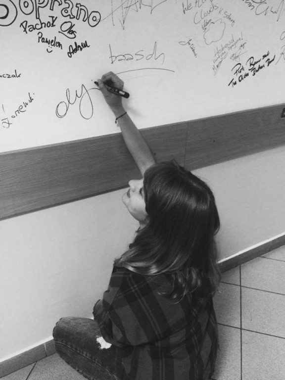 Czarno-białe zdjęcie siedzącej kobiety piszącej na ścianie markerem 'oly'