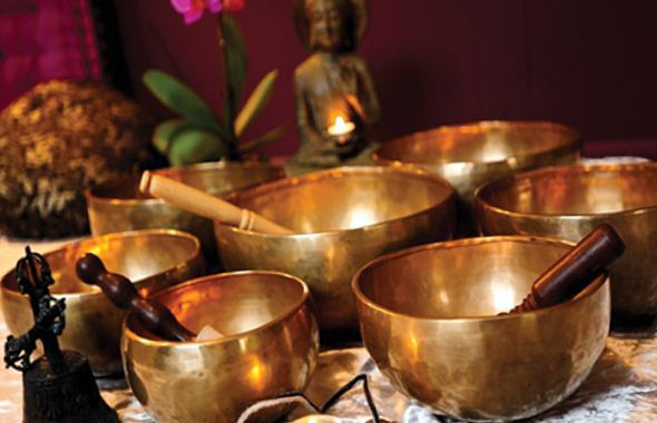 Metalowe, złote miski, za nimi mały posążek z Buddą i kwiatek