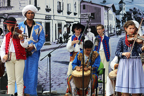 Grupa ludzi ubranych w tradycyjne słowiańskie i afrykańskie stroje gra na instrumentach na rynku