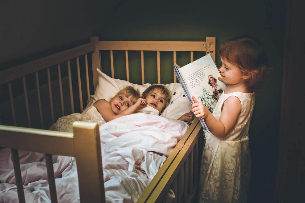 dwie dziewczynki w łóżku dziecięcym, trzecia czyta im bajkę