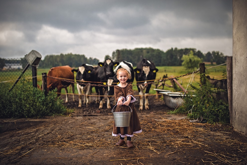 Dziewczynka z wiaderkiem na tle krów i wiejskiego krajobrazu