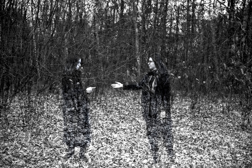 Dwie dziewczyny w lesie za krzakami, jedna z telefonem, druga wyciąga po niego ręke