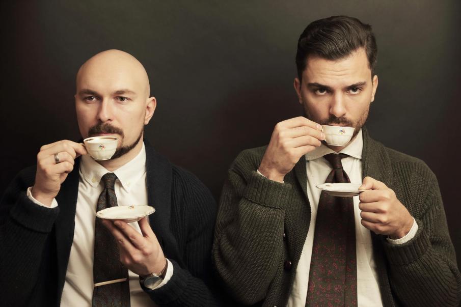 Dwóch mężczyzn pijących kawę z filiżanek i trzymających talerze