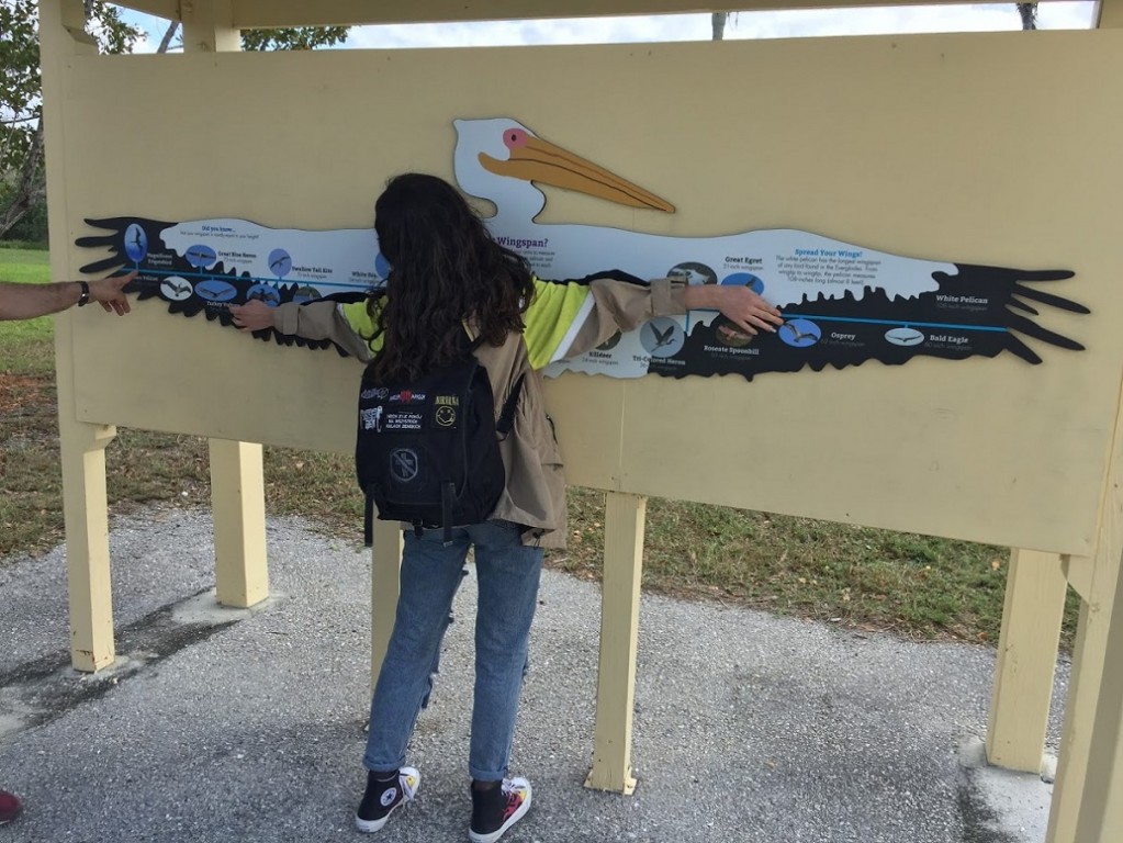 Kobieta z rozwartymi ramionami przykładająca ręce do malowidła z bocianem z rozłożonymi skrzydłami