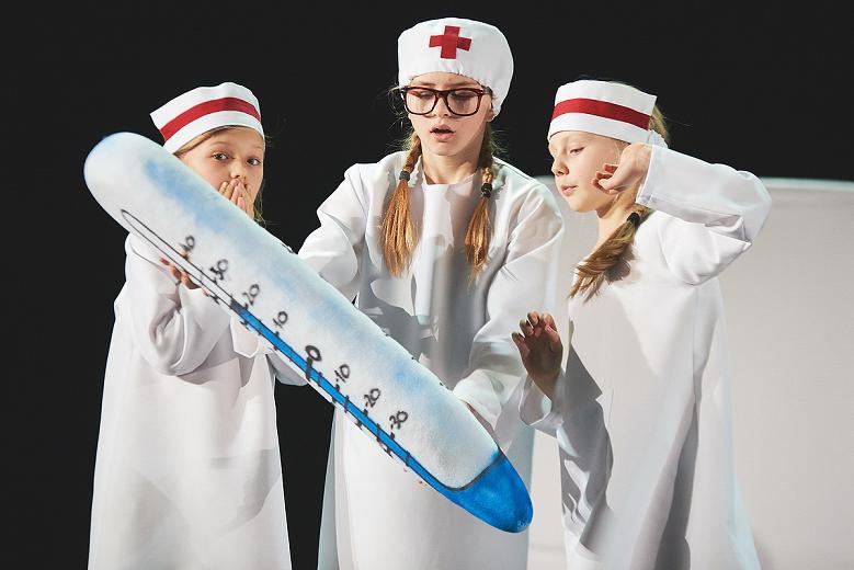 Trzy dziewczynki przebrane za lekarzy trzymają duży, metrowy termometr