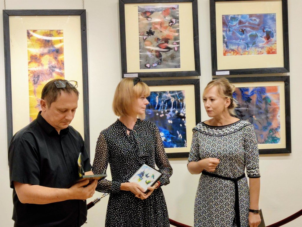 Organizatorka wystawy przedstawia gości wieczoru - duet muzyczny Karolinę i Jarosława Hanik tle prac w Galerii Kolumnowej
