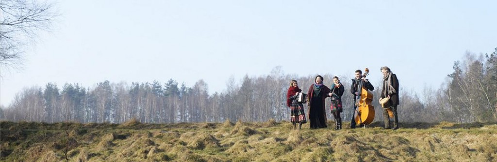 Zespół muzyczny stojący na tle polany, za nimi las