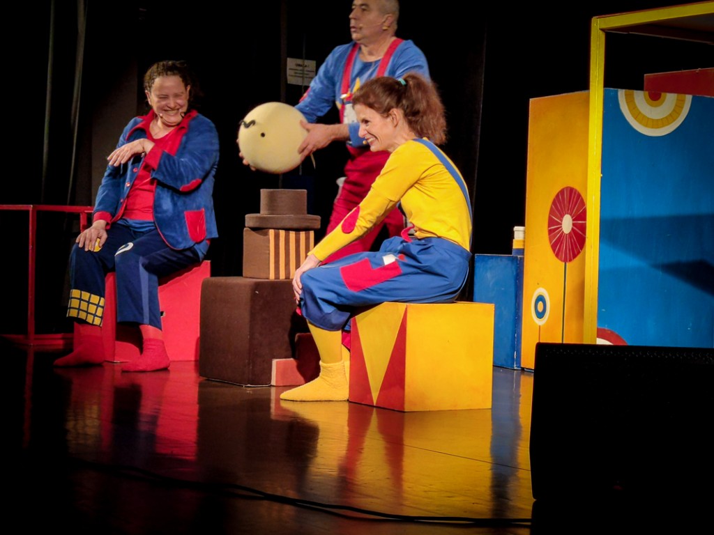 trójka aktorów siedzi na kolorowych kostkach na scenie
